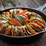 Piękne francuskie jedzenie: ratatouille w żeliwnej patelni, z plastrów cukinii, bakłażana i pomidorów, doprawione ziołami.