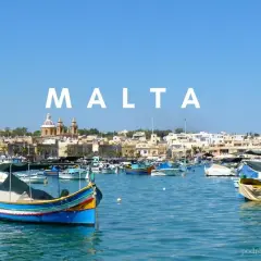 Kolorowe łodzie rybackie w porcie, z miastem i kościołem w tle. Malta historia wita żeglarzy.