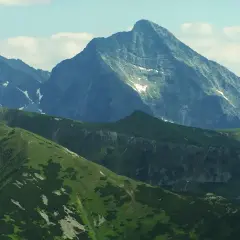 Majestatyczny szczyt w Tatrach Wysokich 2494 m, otoczony zielonymi grzbietami i skalistymi zboczami, z resztkami śniegu.