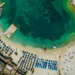 Albania, idealne miejsce na wakacje! Widok z lotu ptaka na turkusową wodę, piaszczystą plażę z leżakami i parasolami, drewniane molo i łodzie.