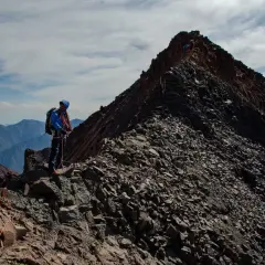 Alpinista na grani, zbliża się do najwyższego szczytu Gruzji. W tle górzyste krajobrazy.