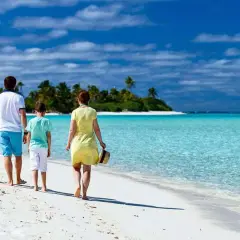 Rodzina cieszy się wakacjami z dziećmi za granicą, spacerując po rajskiej plaży z turkusową wodą i palmami w tle.