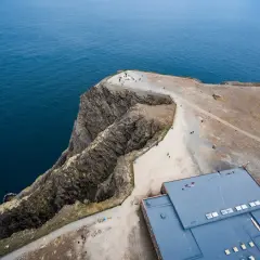 Widok z lotu ptaka na klifowe wybrzeże i budynek przy Nordkapp. Turyści podziwiają ocean.