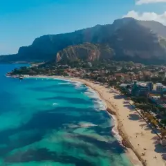 Piękna plaża z turkusową wodą i górami w tle. Ludzie spacerują, odpoczywają. Czy na Sycylii jest bezpiecznie? Tak, wygląda na spokojne miejsce.