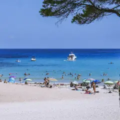 Słoneczna plaża na Balearach, ludzie opalają się i kąpią w turkusowym morzu.