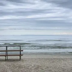 Pusta ławka na plaży, morze i chmury. Idealne miejsce na orzechowo-czekoladowe lody.