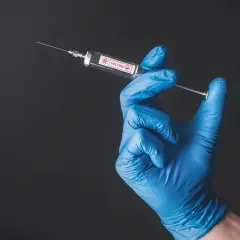 Ręka w niebieskiej rękawiczce trzyma strzykawkę z napisem "VACCINE". To symbol nadziei na bezpieczne podróże, np. do Tunezji, gdzie tunezja szczepienia są ważne.