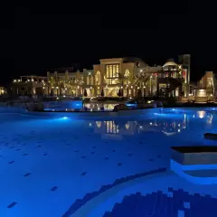 Nocny basen z niebieskim podświetleniem i luksusowym hotelem Lazuli w tle.