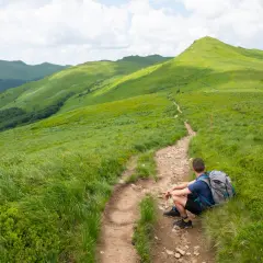 Turysta odpoczywa na szlaku, podziwiając zielone połoniny i łagodne bieszczady szczyty.