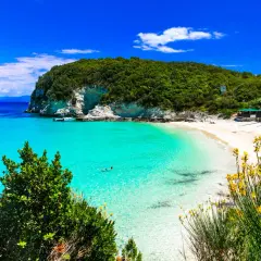 Rajska plaża na Paxos i Antipaxos. Turkusowa woda, biały piasek, zielone wzgórza i żółte kwiaty tworzą idylliczny krajobraz.