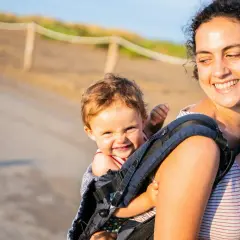 Uśmiechnięta mama niesie dziecko w nosidle. Radosne wakacje z niemowlakiem na spacerze.