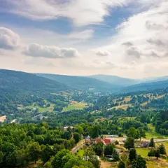 Malowniczy krajobraz Gór Izerskich z zielonymi dolinami, lasami i domkami. Idealne miejsce na odkrywanie szlaków.