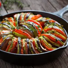 Piękne francuskie jedzenie: ratatouille w żeliwnej patelni, z plastrów cukinii, bakłażana i pomidorów, doprawione ziołami.