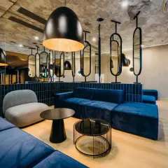 Nowoczesne wnętrze z niebieskimi sofami i szarym fotelem. Stylowe lampy i lustra tworzą atmosferę godną 4-gwiazdkowego hotelu.
