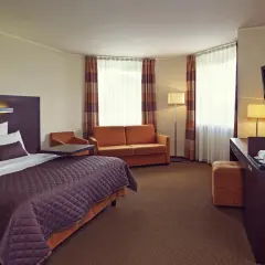 Przytulny pokój w hotelu Mercure Warszawa Airport: łóżko, kanapa, biurko z ekspresem do kawy i TV.