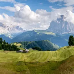 Zielone wzgórza i drewniane chatki w Val Gardena, z majestatycznymi górami w tle.