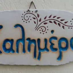 Ceramiczna tabliczka z napisem "Kalimera Grecja" w kolorze niebieskim, ozdobiona greckim wzorem.