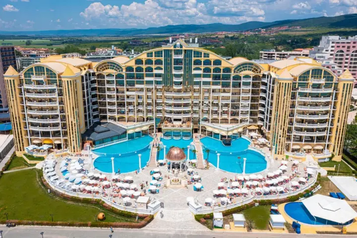 Imperial Palace Hotel z basenami i leżakami, otoczony zielenią i budynkami mieszkalnymi, w słoneczny dzień.