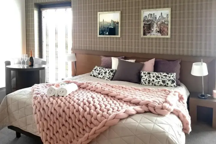 Przytulna sypialnia w hotelu Willowa Lublin. Różowy, gruby pled na łóżku, stolik z szampanem i kieliszkami.