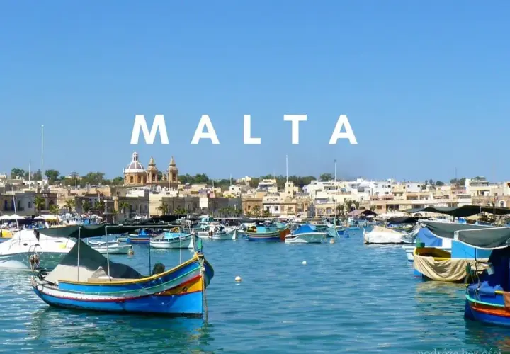 Kolorowe łodzie rybackie w porcie, z miastem i kościołem w tle. Malta historia wita żeglarzy.