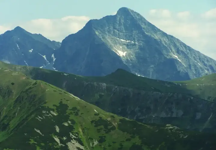 Majestatyczny szczyt w Tatrach Wysokich 2494 m, otoczony zielonymi grzbietami i skalistymi zboczami, z resztkami śniegu.