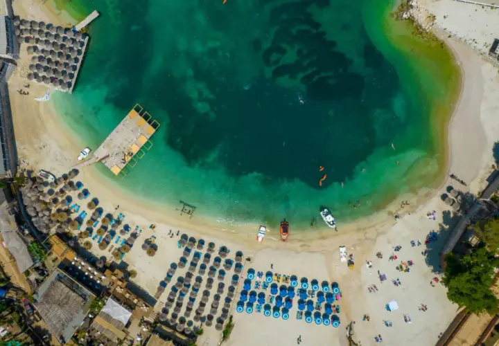 Albania, idealne miejsce na wakacje! Widok z lotu ptaka na turkusową wodę, piaszczystą plażę z leżakami i parasolami, drewniane molo i łodzie.