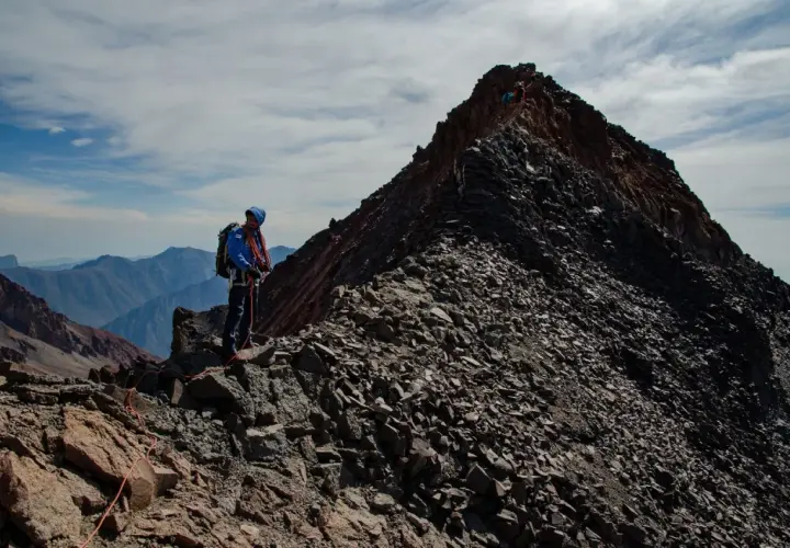 Alpinista na grani, zbliża się do najwyższego szczytu Gruzji. W tle górzyste krajobrazy.
