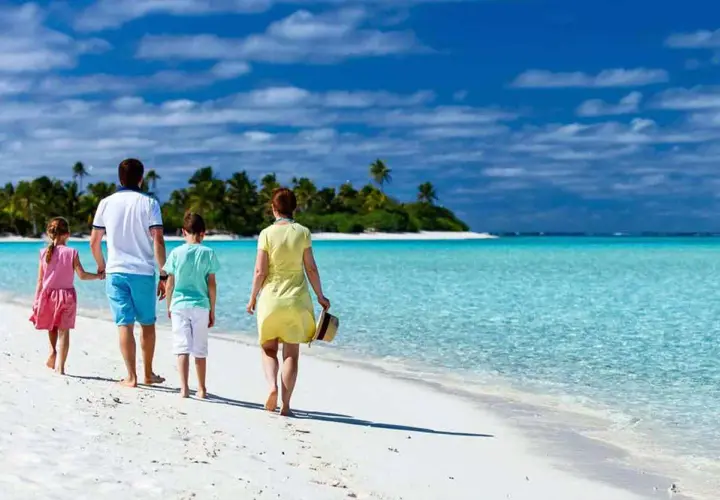 Rodzina cieszy się wakacjami z dziećmi za granicą, spacerując po rajskiej plaży z turkusową wodą i palmami w tle.