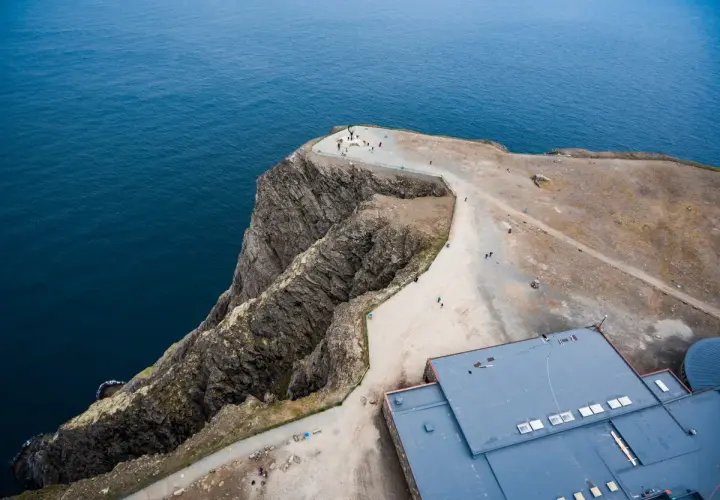 Widok z lotu ptaka na klifowe wybrzeże i budynek przy Nordkapp. Turyści podziwiają ocean.