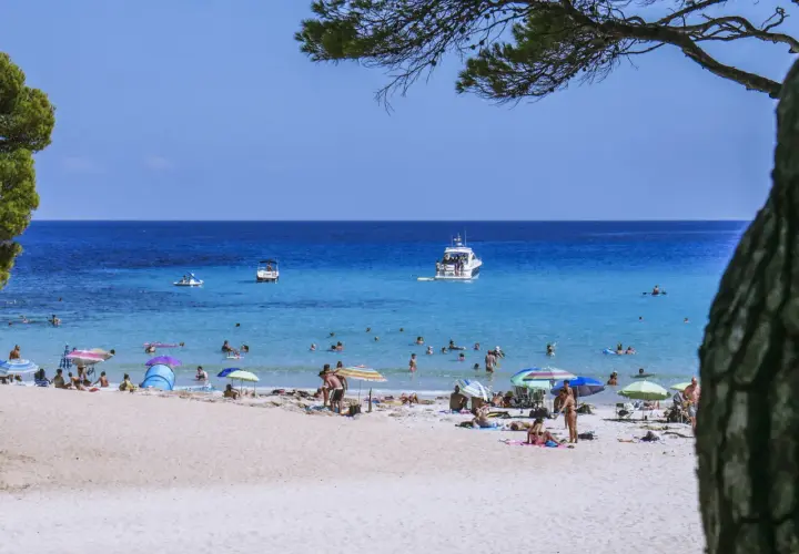 Słoneczna plaża na Balearach, ludzie opalają się i kąpią w turkusowym morzu.
