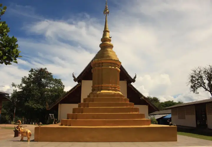 Złota pagoda, symbol buddyzmu, wznosi się na tle błękitnego nieba. Obok stoi złoty słoń.