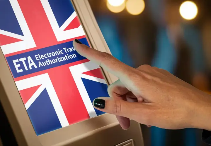 Dłoń dotyka ekranu z flagą Wielkiej Brytanii i napisem ETA. Czy Polacy potrzebują wizy do Wielkiej Brytanii? ETA to elektroniczne zezwolenie na podróż.