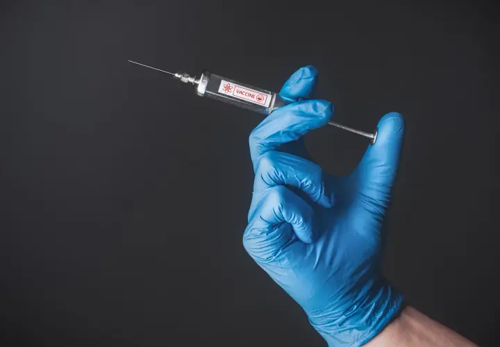 Ręka w niebieskiej rękawiczce trzyma strzykawkę z napisem "VACCINE". To symbol nadziei na bezpieczne podróże, np. do Tunezji, gdzie tunezja szczepienia są ważne.
