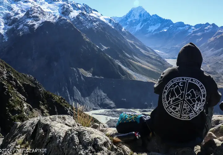 Osoba w bluzie z napisem "Into the Wild" patrzy na najwyższy szczyt Nowej Zelandii, Aoraki/Mount Cook.