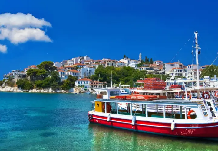 Skopelos wakacje: białe domy na wzgórzu, turkusowa woda i łodzie w porcie. Idealne miejsce na greckie wakacje.
