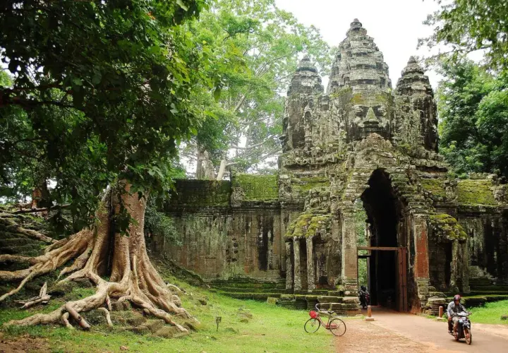 Wspaniałe kamienne twarze Angkor Thom witają na kambodżańskie wakacje. Potężne korzenie drzew oplatają starożytne mury.