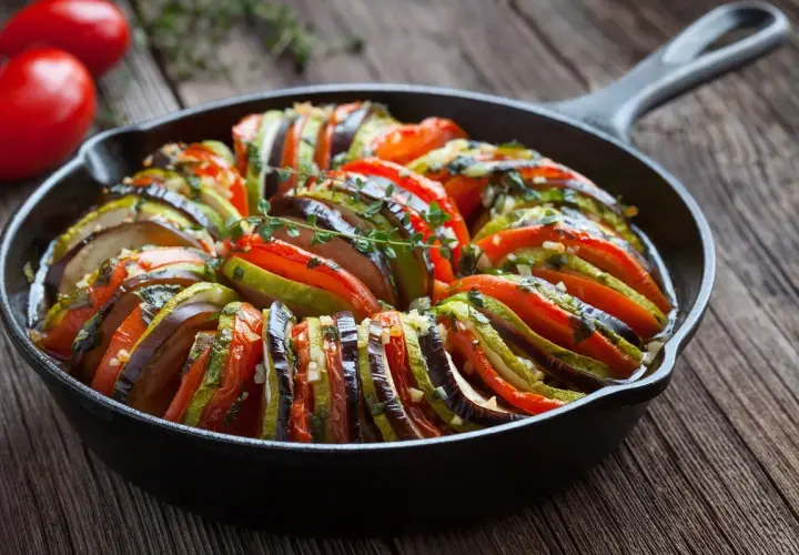Piękne francuskie jedzenie: ratatouille w żeliwnej patelni, z plastrów cukinii, bakłażana i pomidorów, doprawione ziołami.
