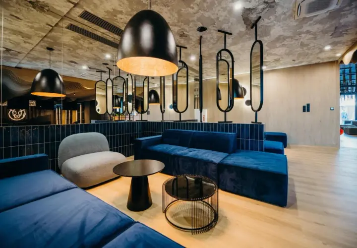 Nowoczesne wnętrze z niebieskimi sofami i szarym fotelem. Stylowe lampy i lustra tworzą atmosferę godną 4-gwiazdkowego hotelu.