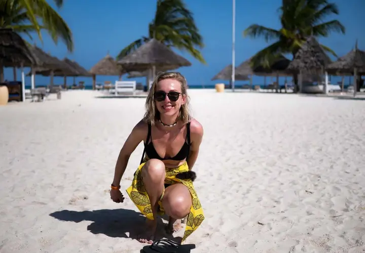 Uśmiechnięta blondynka w bikini i żółtej spódniczce na piaszczystej plaży. Idealne zanzibar wakacje pod palmami.