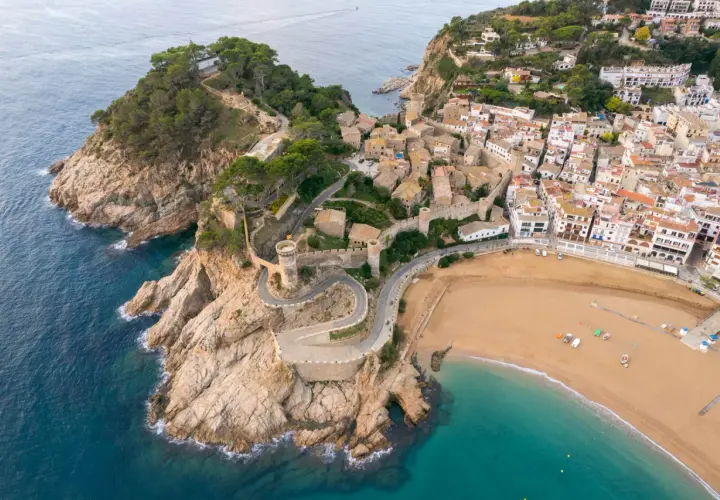 Malownicze widoki na Costa Brava wakacje: miasteczko z zamkiem na klifie, kręta droga i piaszczysta plaża.