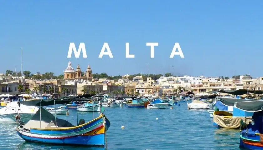 Kolorowe łodzie rybackie w porcie, z miastem i kościołem w tle. Malta historia wita żeglarzy.