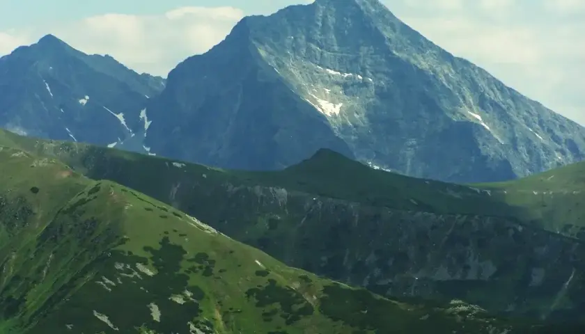 Majestatyczny szczyt w Tatrach Wysokich 2494 m, otoczony zielonymi grzbietami i skalistymi zboczami, z resztkami śniegu.