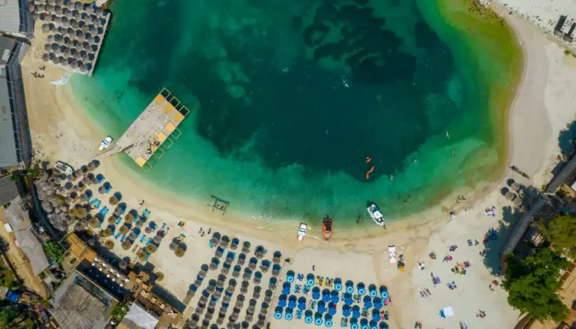 Albania, idealne miejsce na wakacje! Widok z lotu ptaka na turkusową wodę, piaszczystą plażę z leżakami i parasolami, drewniane molo i łodzie.