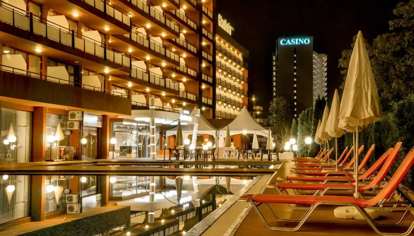 Hotel Gladiola Star nocą, z basenem, leżakami i kasynem w tle.