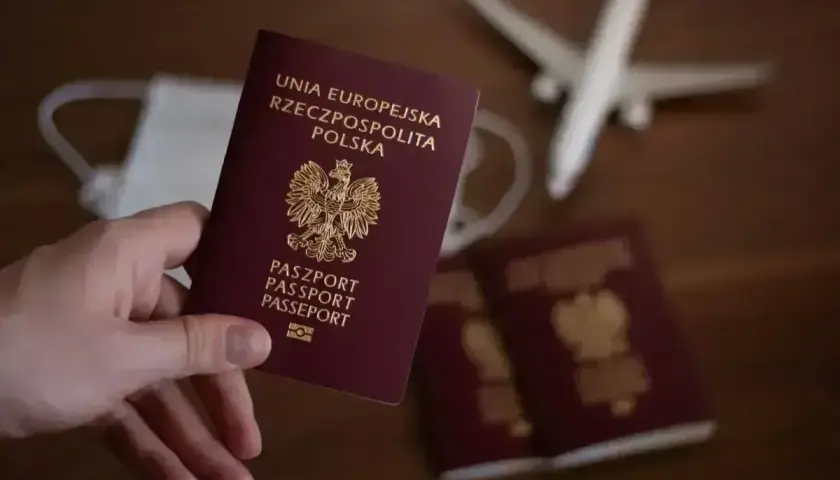 Dłoń trzyma polski paszport. Obok leżą kolejne dokumenty, maseczka i samolot. Czy do Anglii potrzebny jest paszport? Tak, jest niezbędny.