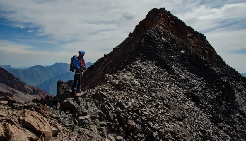 Alpinista na grani, zbliża się do najwyższego szczytu Gruzji. W tle górzyste krajobrazy.