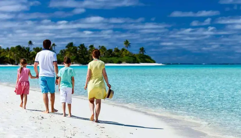 Rodzina cieszy się wakacjami z dziećmi za granicą, spacerując po rajskiej plaży z turkusową wodą i palmami w tle.