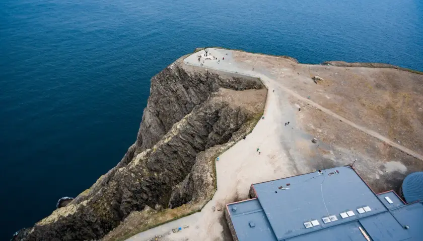 Widok z lotu ptaka na klifowe wybrzeże i budynek przy Nordkapp. Turyści podziwiają ocean.