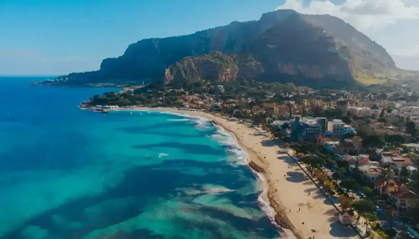 Piękna plaża z turkusową wodą i górami w tle. Ludzie spacerują, odpoczywają. Czy na Sycylii jest bezpiecznie? Tak, wygląda na spokojne miejsce.