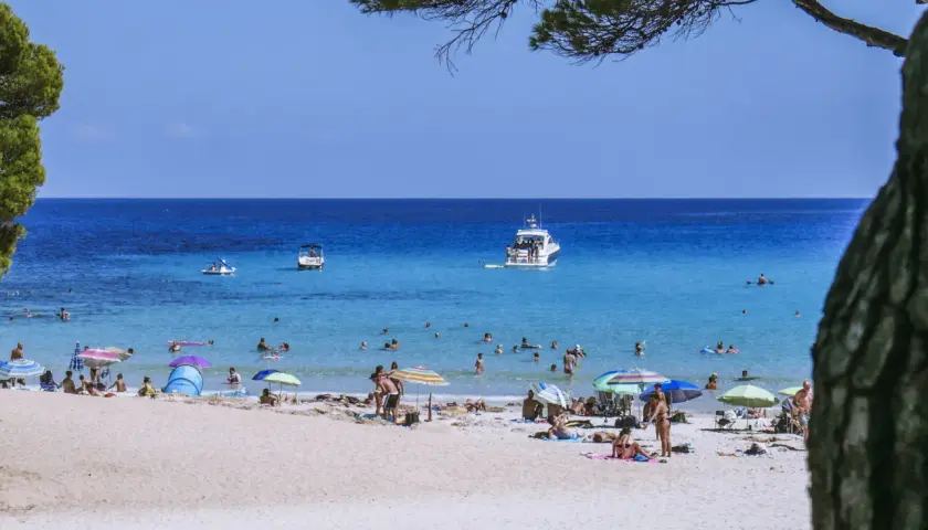 Słoneczna plaża na Balearach, ludzie opalają się i kąpią w turkusowym morzu.